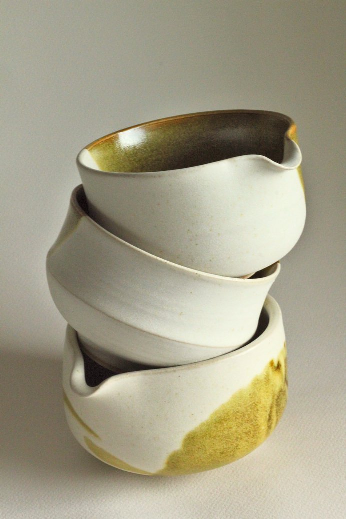 A stack of stoneware matcha bowls with white and mossy green glaze.