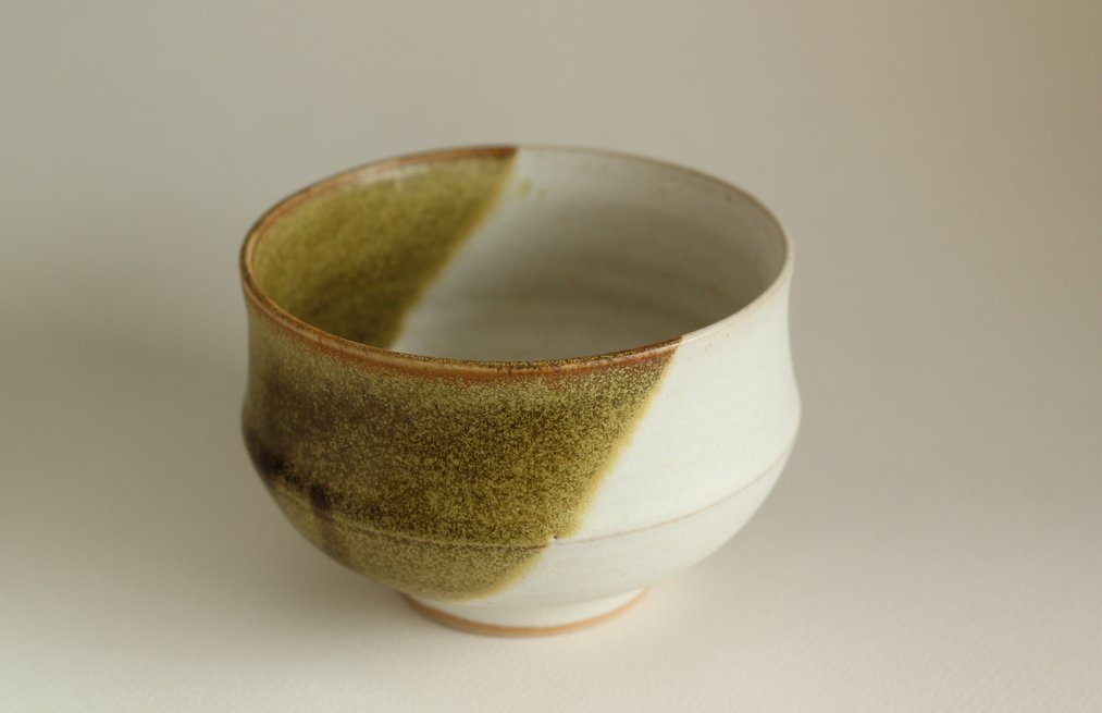 A small stoneware bowl with white and mossy green glaze.
