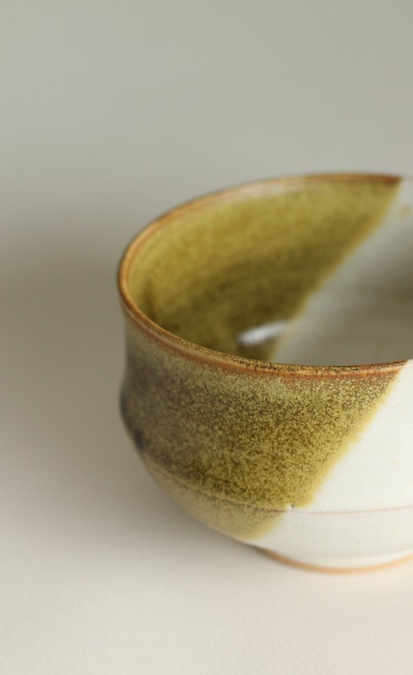 Closeup of small stoneware bowl with white and mossy green glaze.